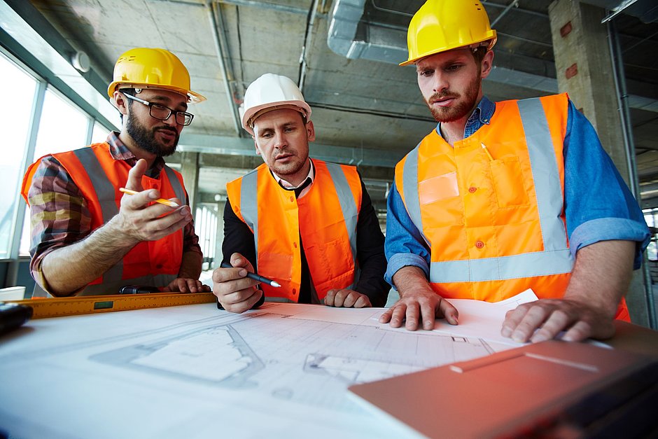 Drei Bauingenieure an einem Tisch diskutieren über einen Bauplan